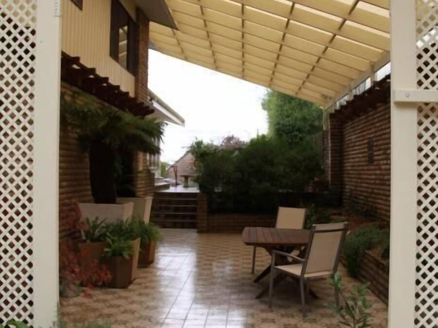 A covered patio area with a tiled floor, a table and chairs, and potted plants.