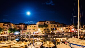 Un puerto deportivo con barcos amarrados, una luna en el cielo y edificios con terrazas.