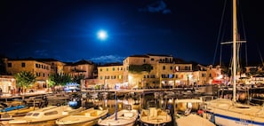 Un port de plaisance avec des bateaux amarrés, une lune dans le ciel et des bâtiments dotés de terrasses extérieures.