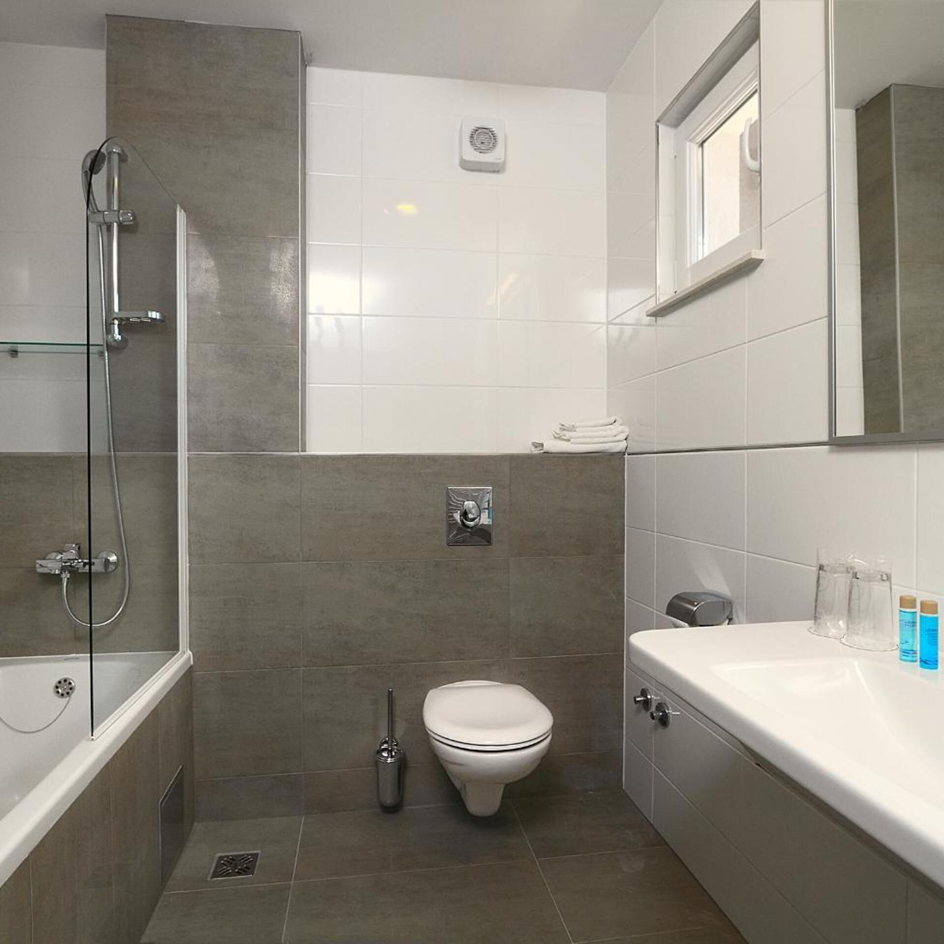 Une salle de bain équipée d’une douche, de toilettes et d’un lavabo, avec des carreaux gris et un plan de toilette blanc.