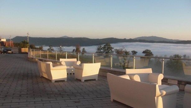 Une terrasse sur le toit, dotée de mobilier d’extérieur blanc et offrant une vue sur un lac et des montagnes.