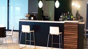 Un espace bar moderne avec deux tabourets, un comptoir et des luminaires suspendus.