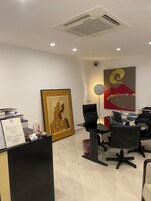 Un moderno spazio ufficio con una scrivania di accoglienza, sedie da ufficio nere, un grande quadro astratto e un condizionatore d'aria a parete.