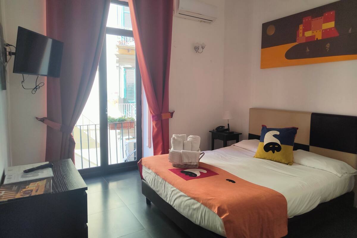 A hotel room with a bed, a desk, a chair, a TV, and a window with curtains.