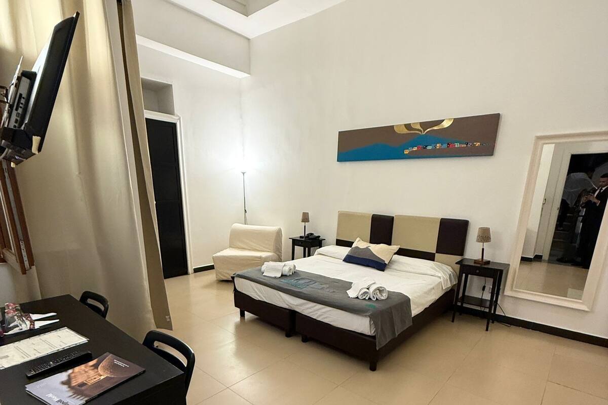 A hotel room with a bed, a desk, a chair, a lamp, and a painting on the wall.