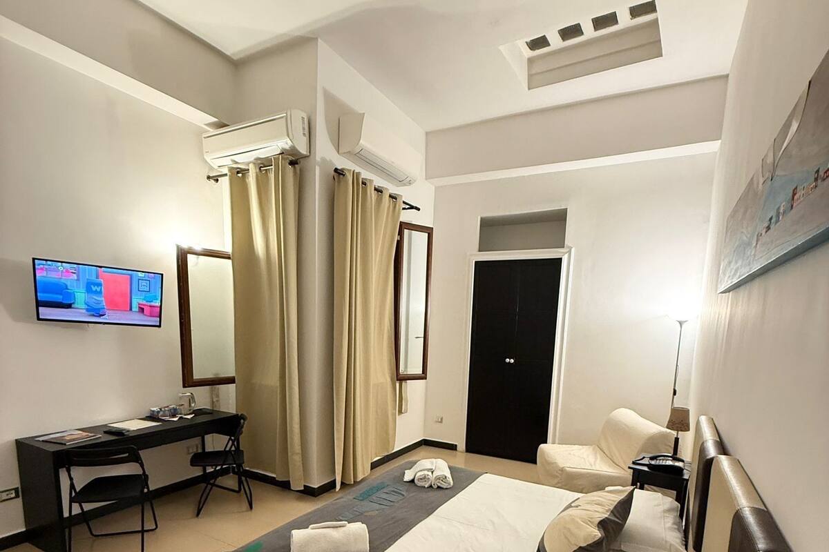A hotel room with a bed, a desk, a chair, a TV, a door, and a lamp.