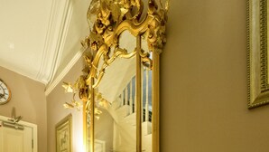 An ornate wooden console table with a large mirror, a lamp, and a vase with flowers. - Cheshire Hospitality Ltd T/A Lennox Lea Studios & Apartments (Sale)