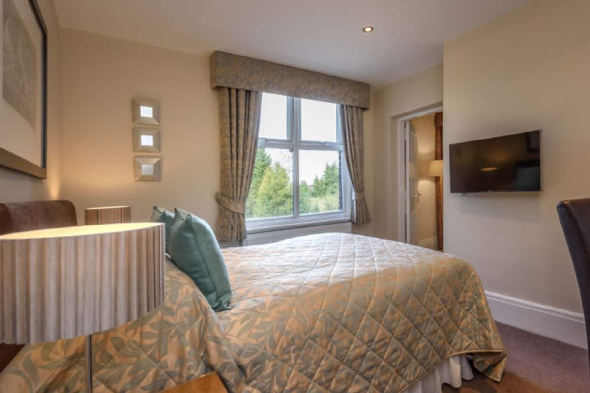 A bedroom with a bed, a chair, a TV, and a window with curtains.