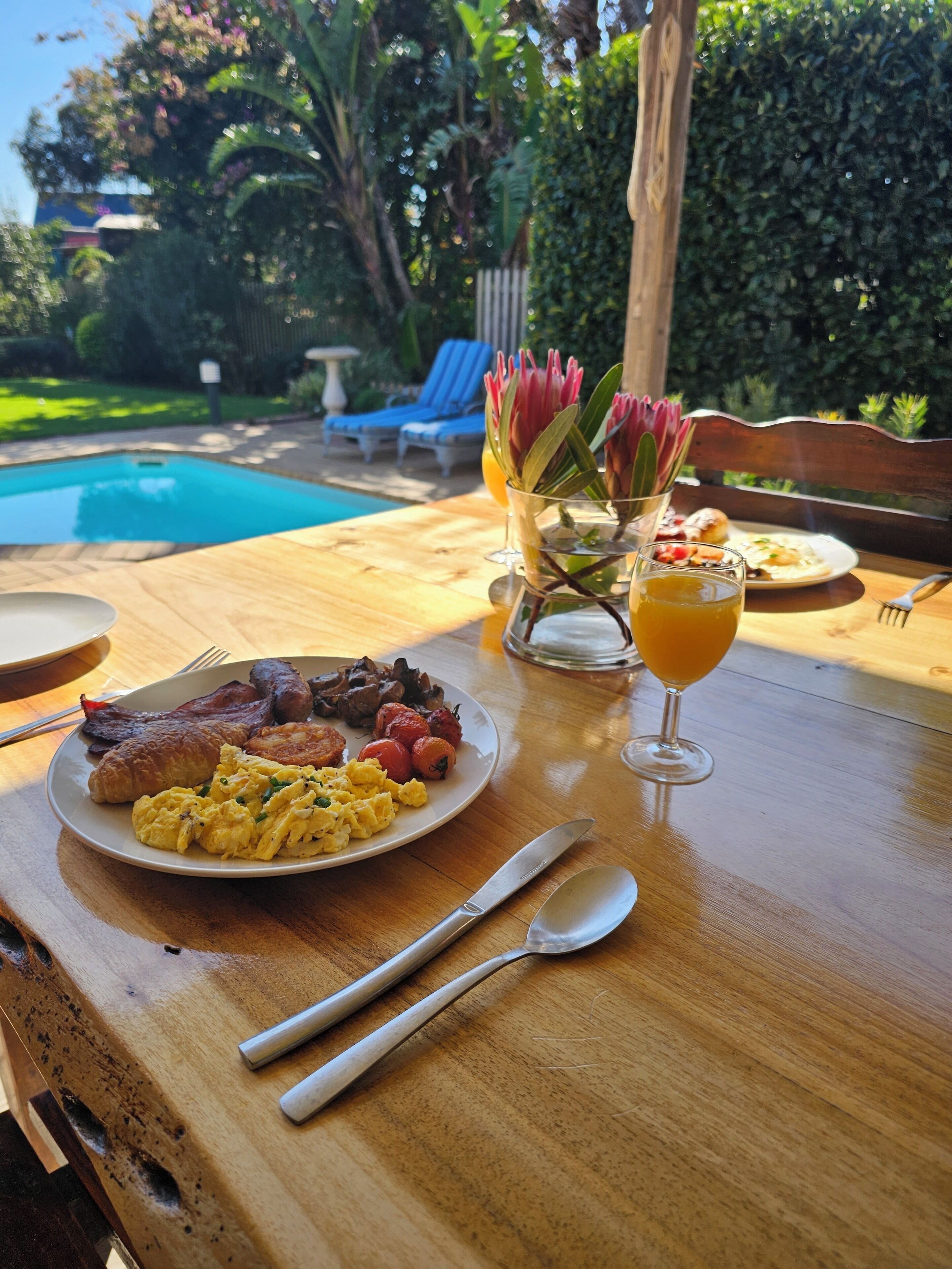 Une table à manger avec des assiettes pour le petit-déjeuner, des couverts et un verre de jus d’orange.