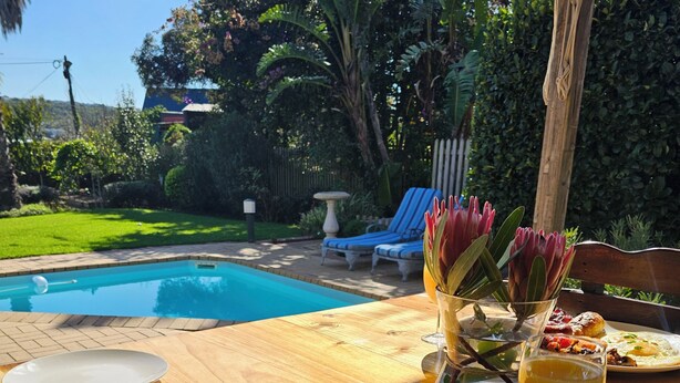 Et morgenbord med mad, et glas appelsinjuice og udsigt til en swimmingpool og have.