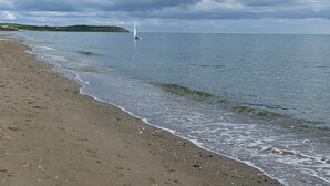 A beach with a sailboat in the distance, calm sea, and overcast sky. - Flynns of Termonfeckin (Termonfeckin)