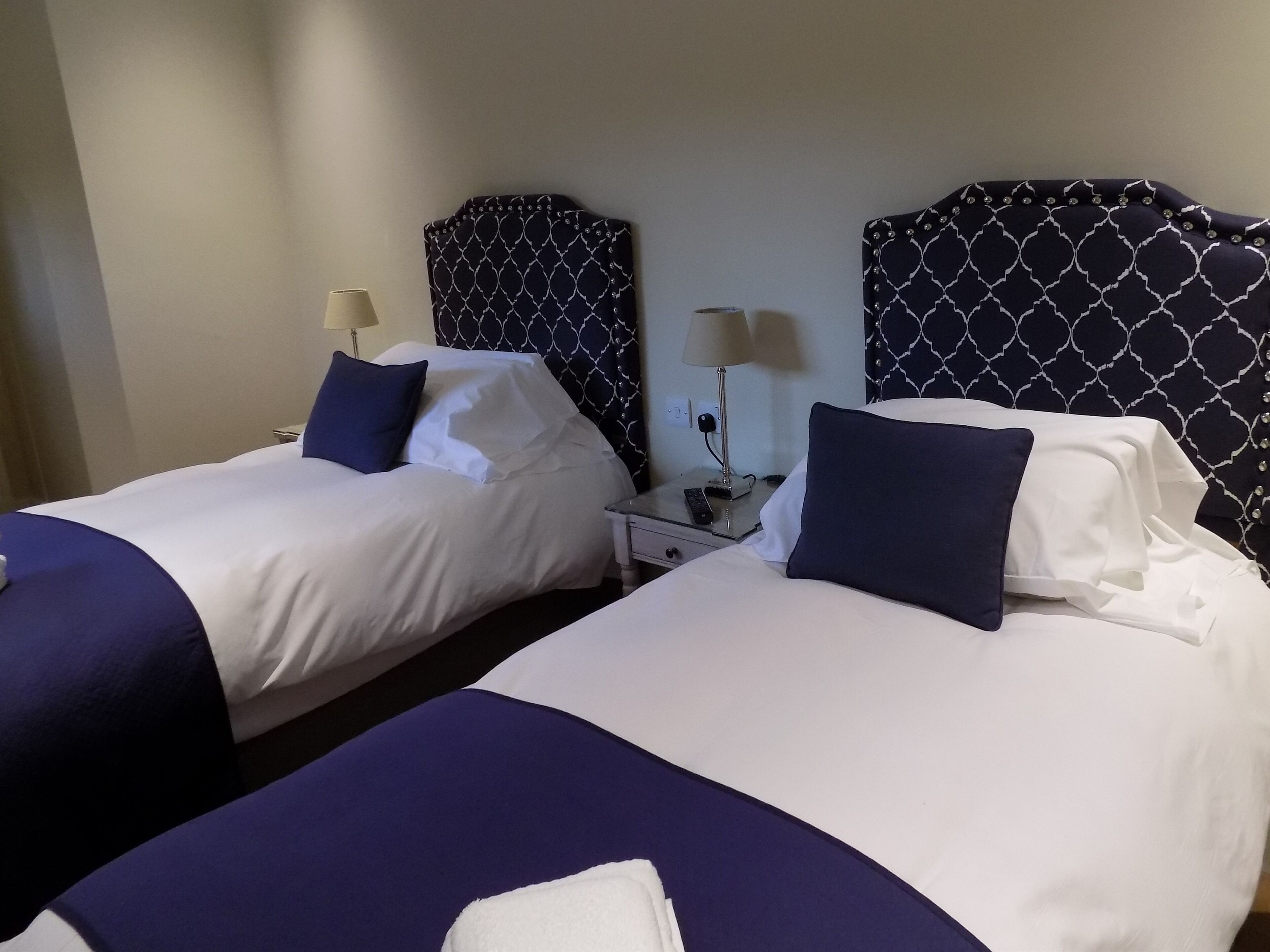 A hotel room with two beds, each with a headboard, bedside tables, lamps, and pillows.