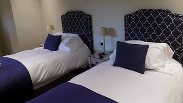 Quarto de hotel com duas camas, cada uma com cabeceira, mesas de cabeceira, abajures e almofadas.
