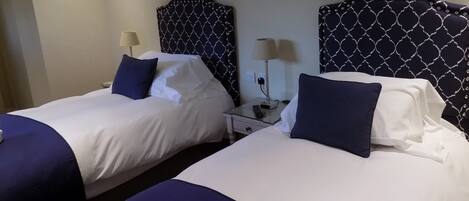 A hotel room with two beds, each with a headboard, bedside tables, lamps, and pillows.