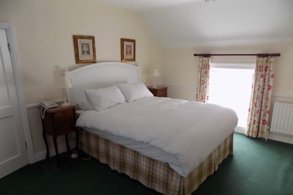 A bedroom with a large bed, two bedside tables, a nightstand, a window with curtains, and two framed pictures on the wall.