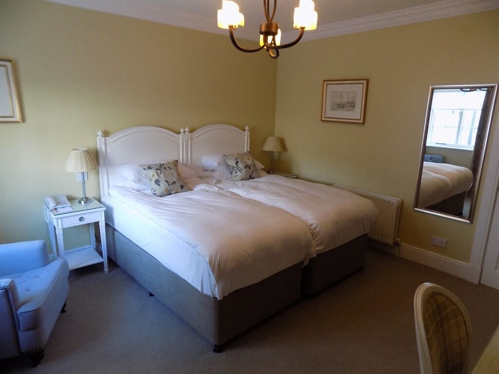 Quarto com cama, mesa de cabeceira, abajur, cadeira e espelho.