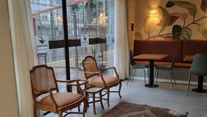 A restaurant with wicker chairs and a table, a patterned rug, and a large window with a view of the street. - Coral Express (Porto Alegre)