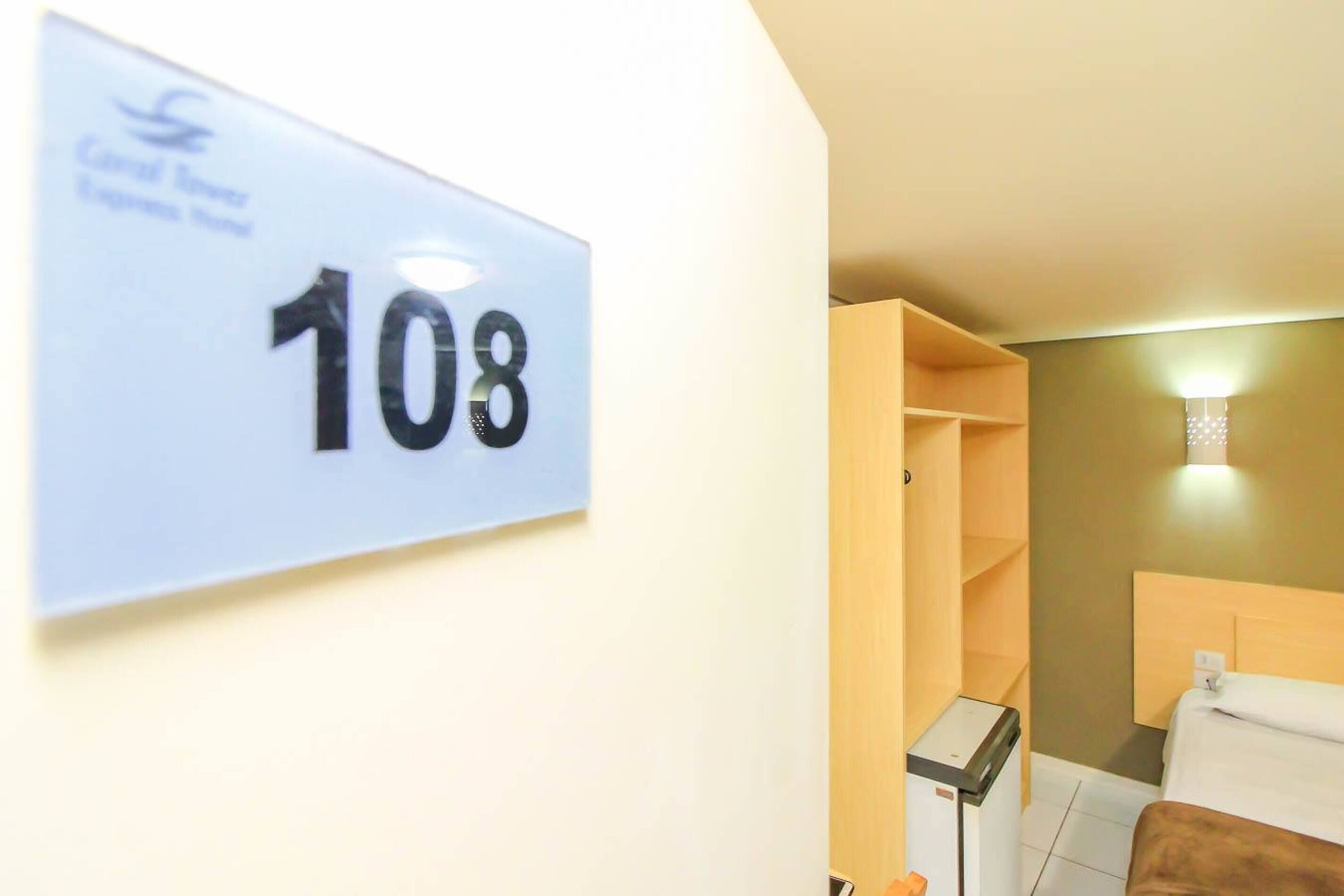 Une chambre d’hôtel avec un panneau indiquant le numéro 108, un lit, une table de chevet et un petit meuble.