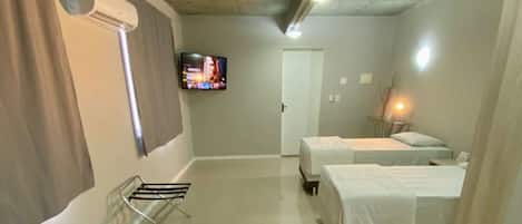A hotel room with two beds, a TV, and a bathroom with a shower.
