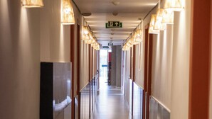 A long, narrow hotel corridor with a central walkway, flanked by walls with doors on both sides. - Coral Express (Porto Alegre)