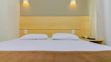 Una cama bien tendida con ropa de cama blanca y dos almohadas, un cabecero de madera y una mesita de noche con un teléfono.