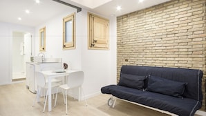 Een moderne woonkamer met een witte eethoek, een donkerblauwe bank en een bakstenen muur.