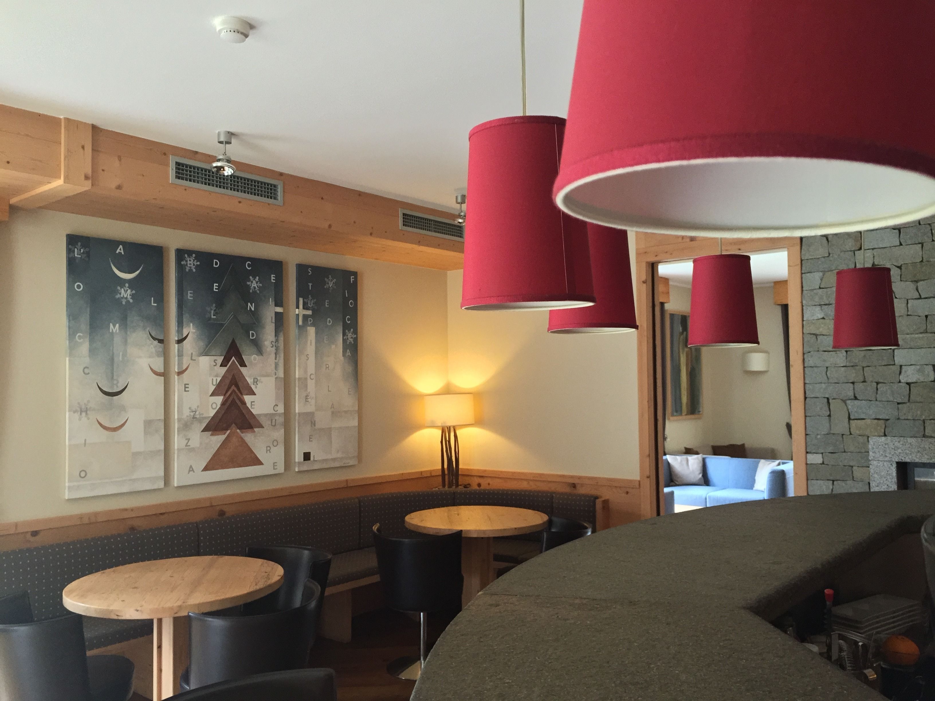A cozy restaurant interior with wooden beams, red pendant lights, and a wall with abstract art.