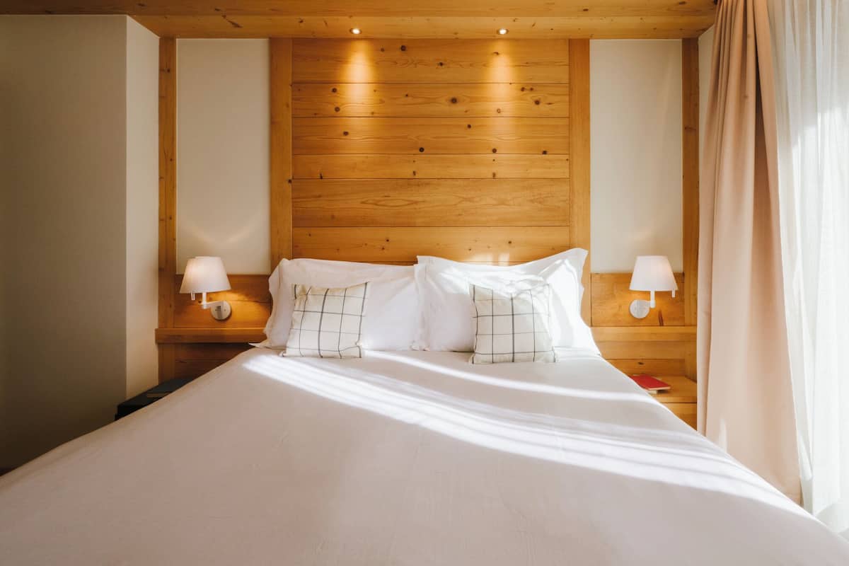 A hotel room with a wooden headboard, two bedside lamps, and a bed with white linens and patterned pillows.