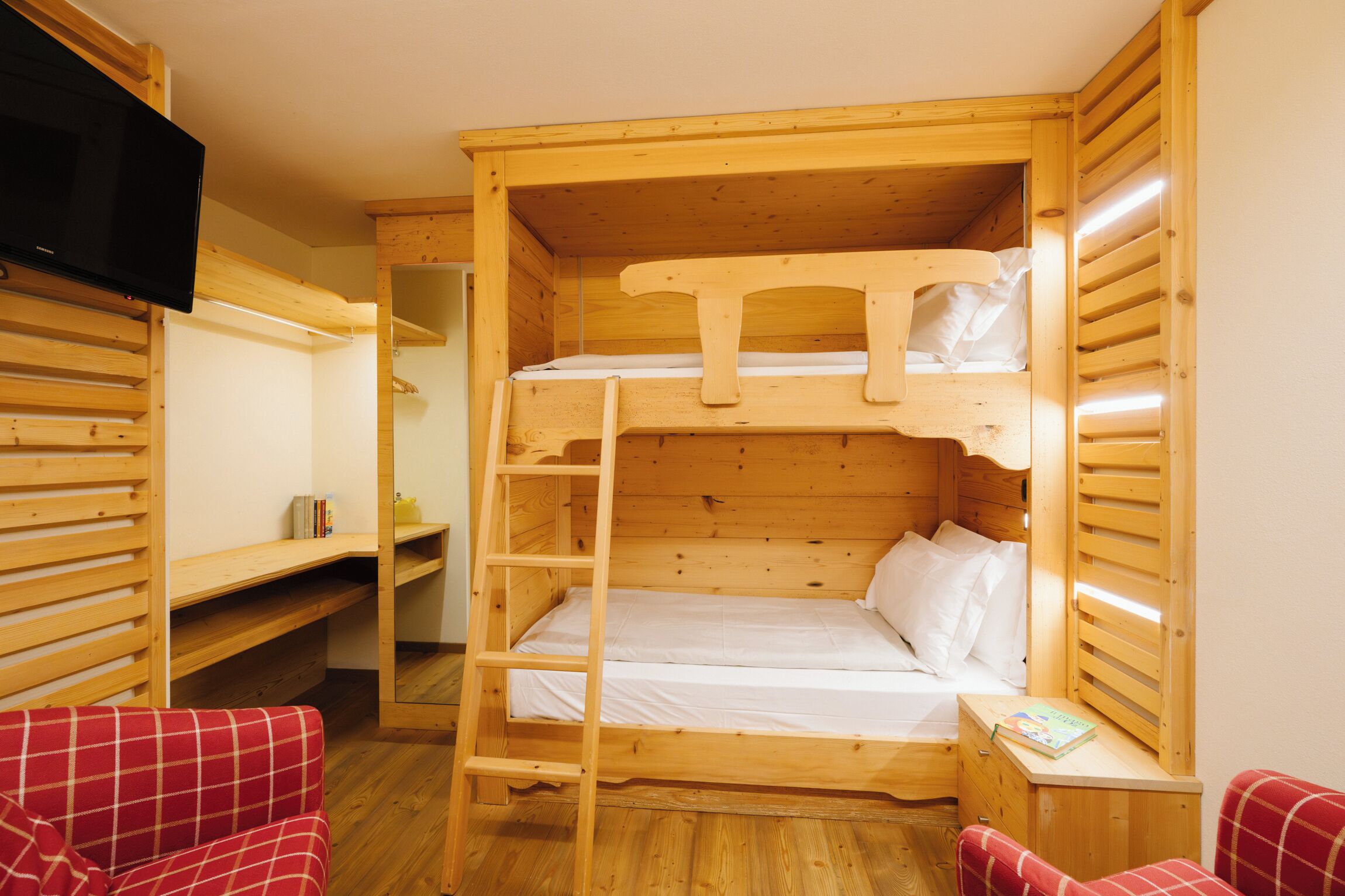 Een slaapkamer met een stapelbed, een televisie aan de muur, een ladder en een klein tafeltje met een boek.