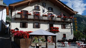 Un hotel con balcón decorado con flores rojas, fachada de madera y cartel que indica que es un hotel.
