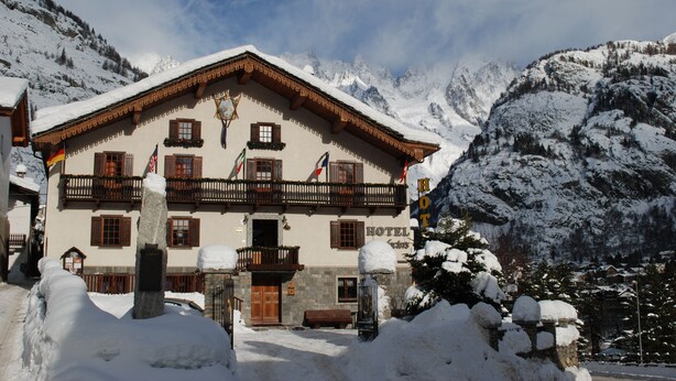 Un hotel de estilo arquitectónico alpino tradicional, con un balcón de madera y fachada cubierta de nieve.