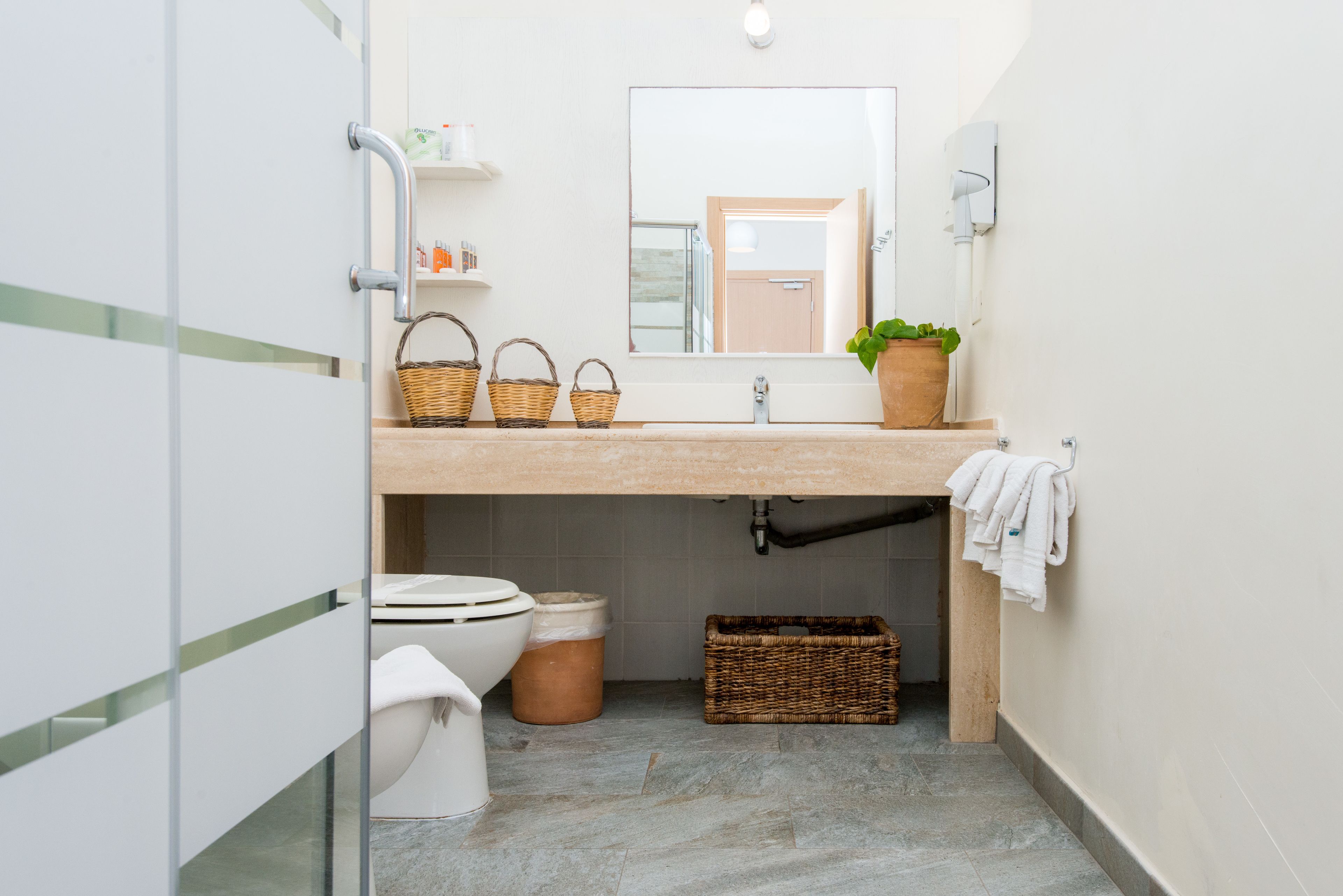 Une salle de bain avec des toilettes, un lavabo et un miroir. On y trouve des paniers et une plante sur le comptoir du lavabo.