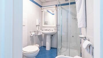 Un baño con inodoro, lavabo y ducha con mampara de vidrio.
