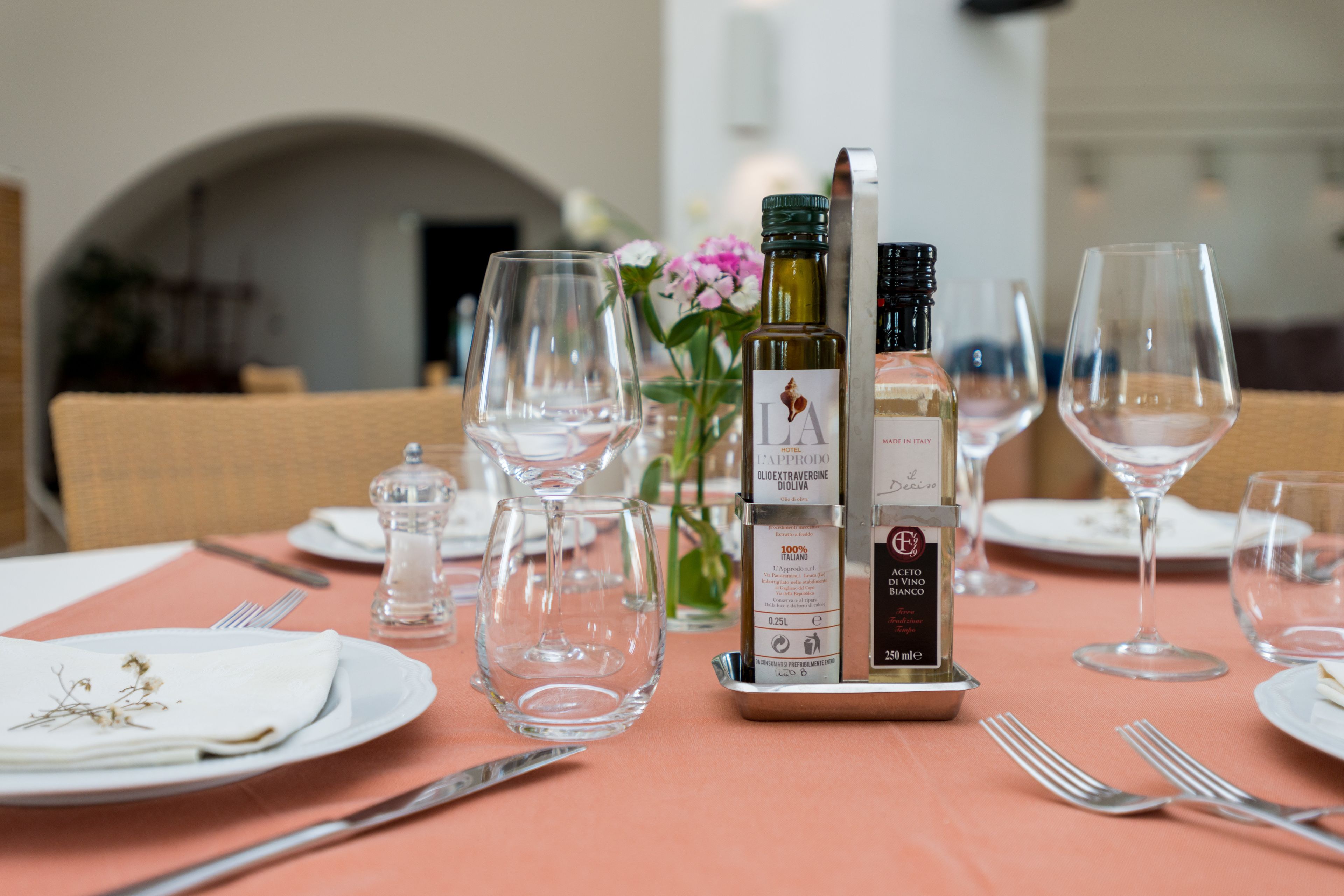 A dining table set with wine glasses, a bottle of olive oil, and a salt shaker.
