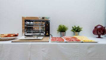 A food station with a grill, various meats, cheese, and bread.