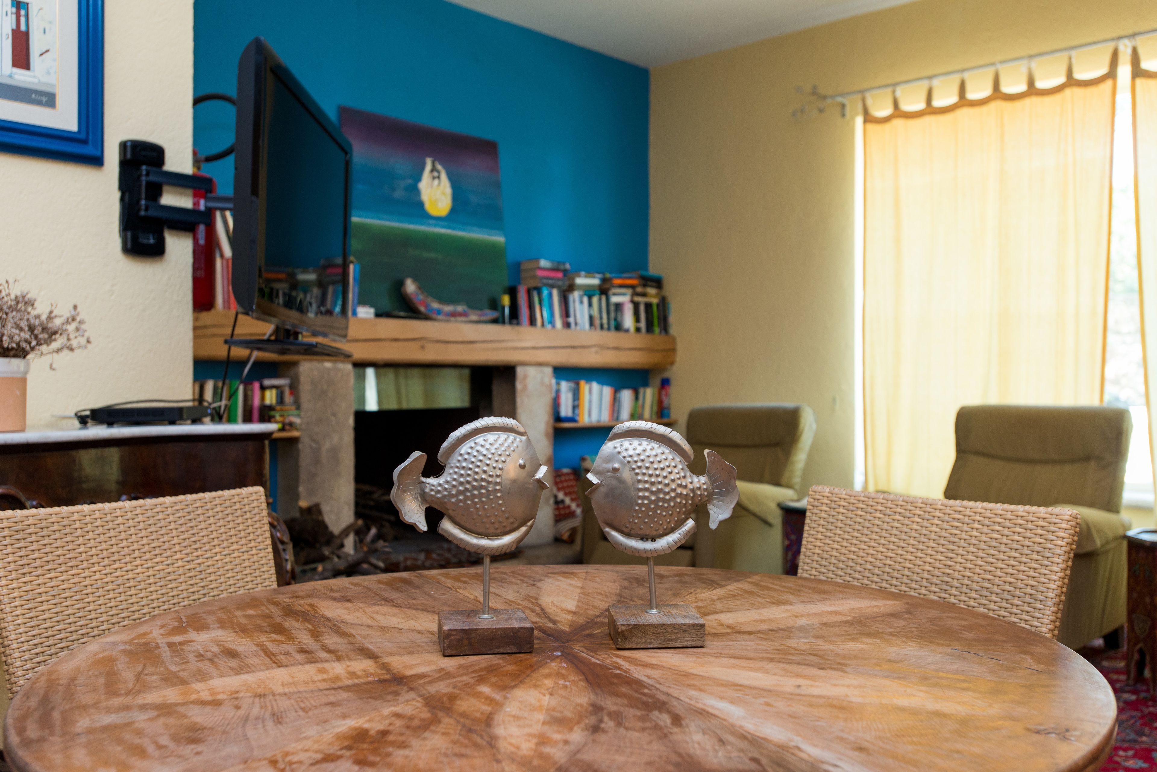 A round wooden table with two fish-shaped sculptures, surrounded by wicker chairs.