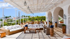 An outdoor seating area with wicker furniture, potted plants, and a pergola with hanging lanterns. - Approdo Boutique Hotel Leuca (Castrignano del Capo)