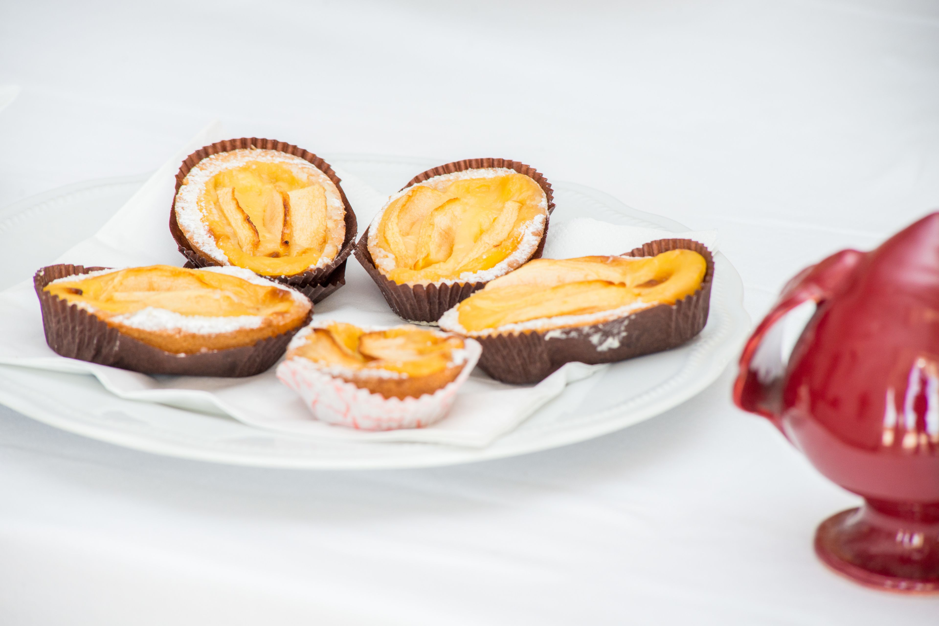 A plate with five chocolate cups containing a yellow filling, a white plate, and a red object in the background.