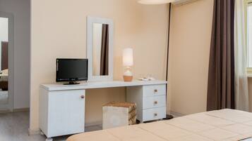 Een hotelkamer met een bed, een bureau met een computer, een spiegel, een lamp en een airconditioner.