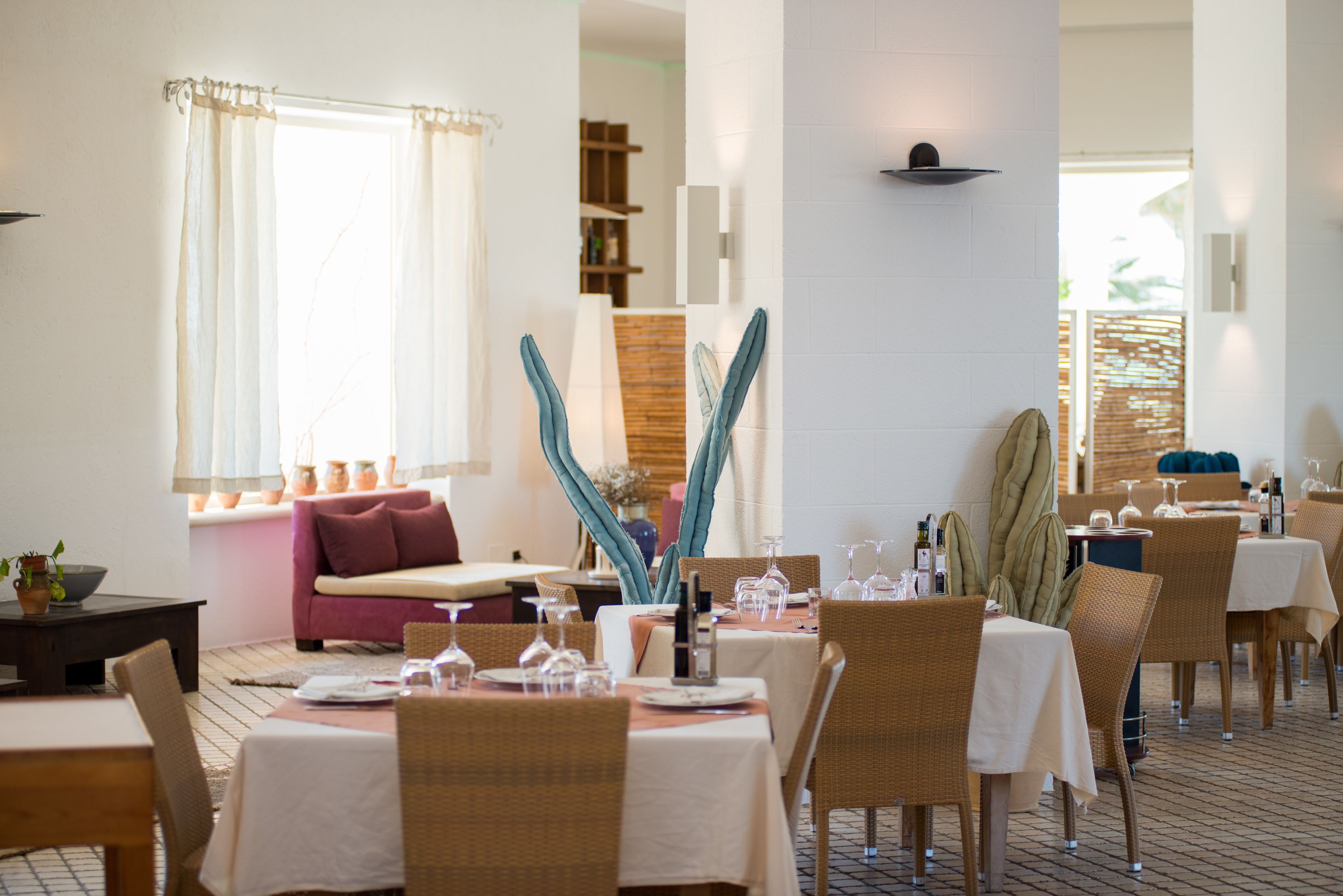 A dining area with tables set for two, wicker chairs, and a sofa with cushions.