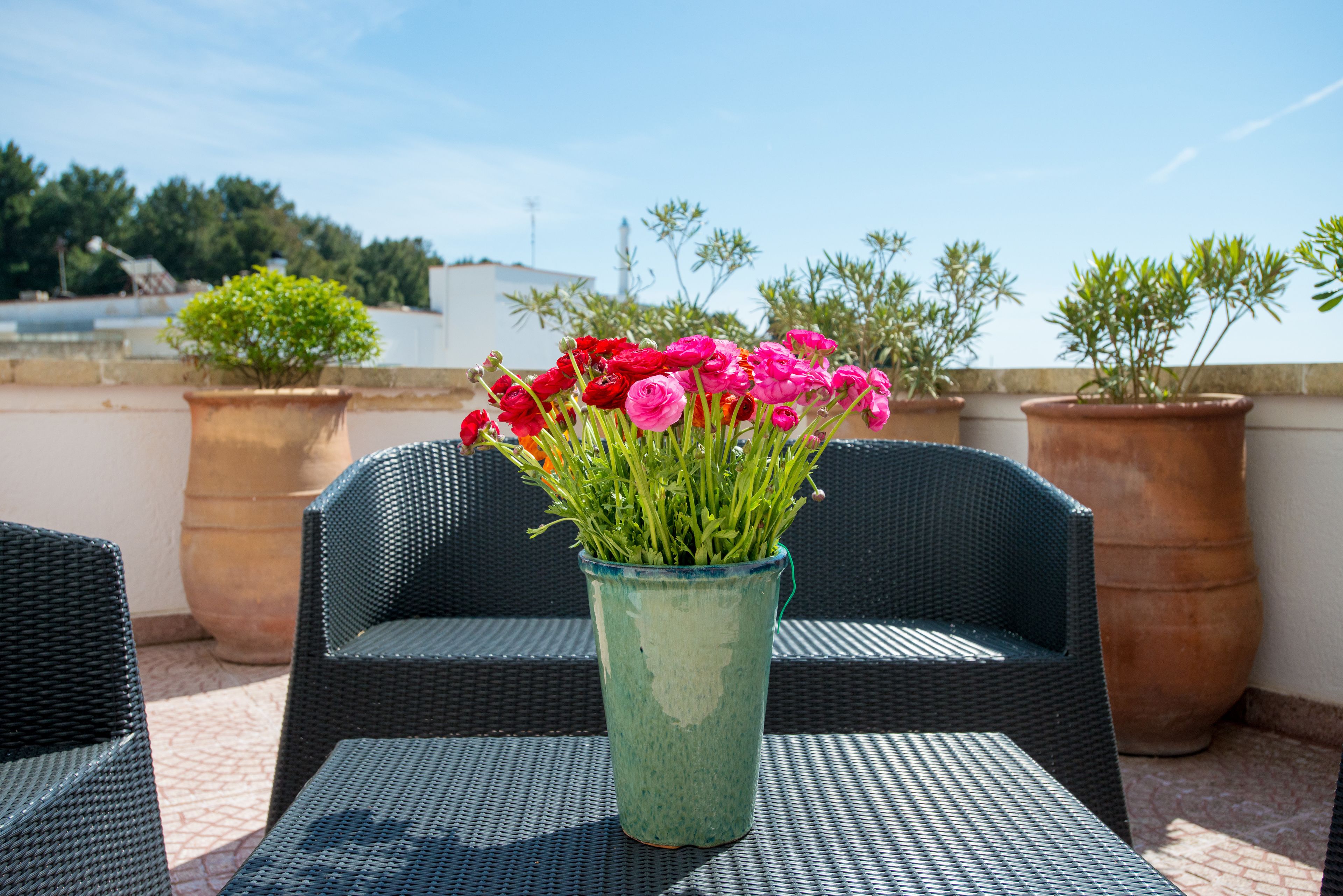 A patio with wicker furniture and a vase of flowers.