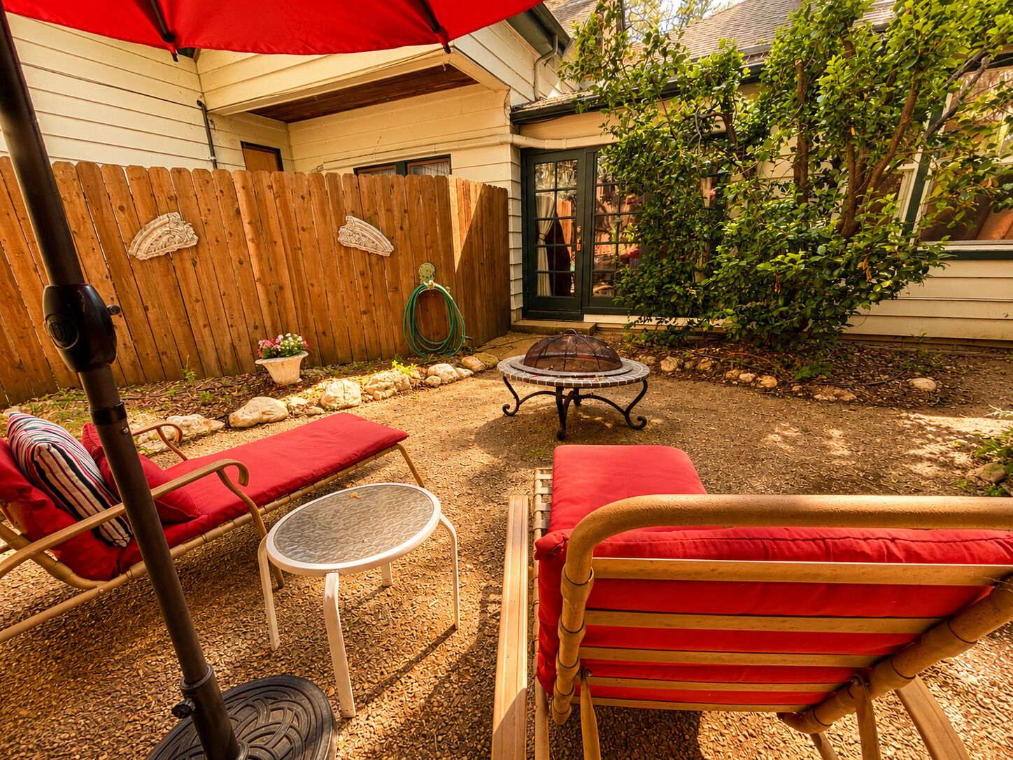 A backyard with a wooden fence, a fire pit, and outdoor furniture including a table and chairs.