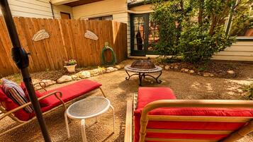 A backyard with a wooden fence, a fire pit, and outdoor furniture including a table and chairs.