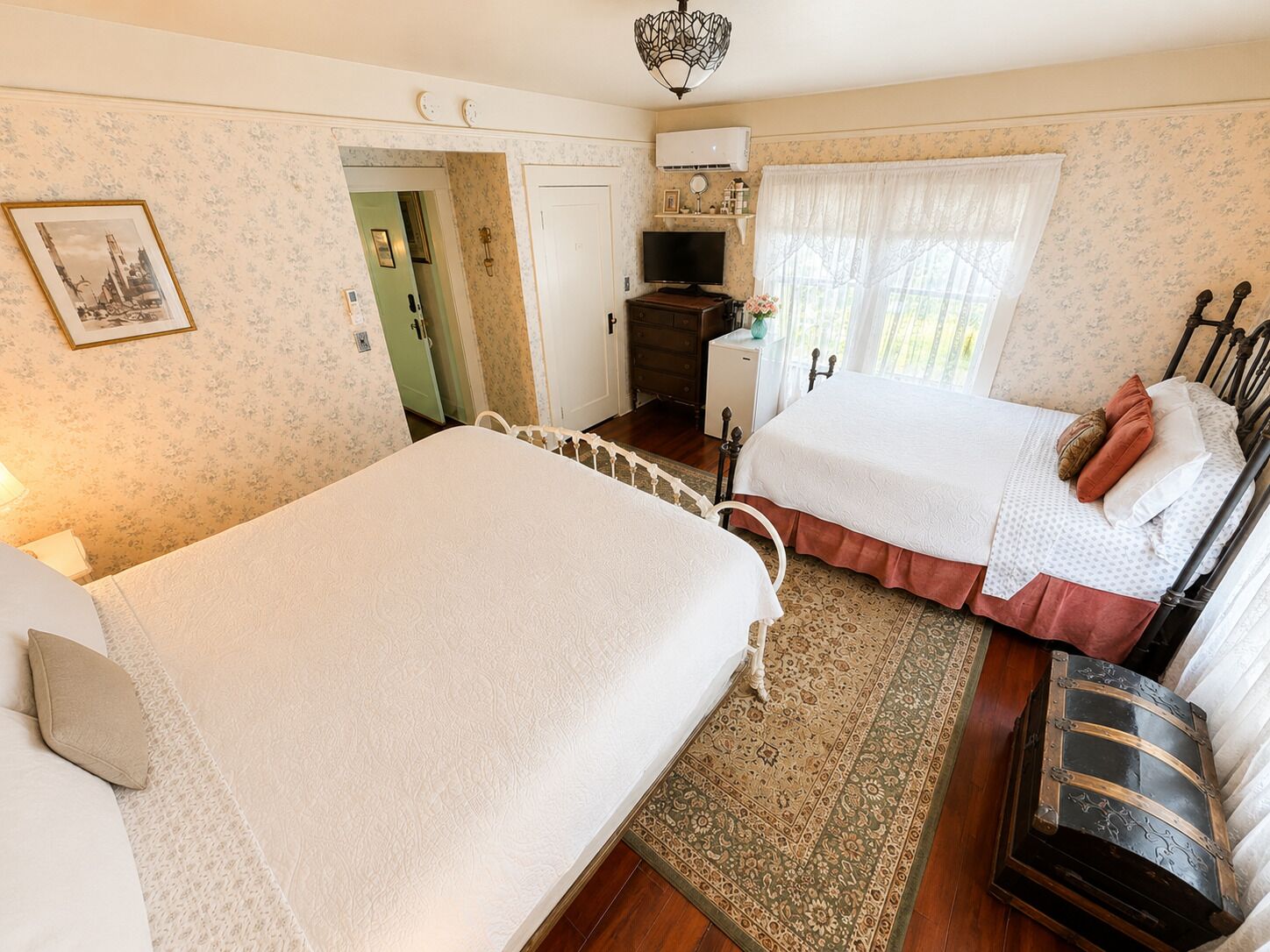 A bedroom with two beds, a dresser, a television, and a chest of drawers.
