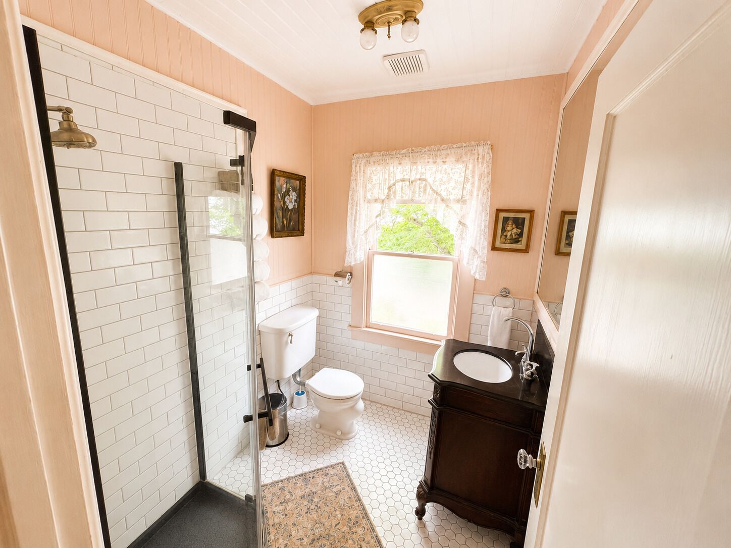 Une salle de bain comprenant des toilettes, un lavabo, une douche et une fenêtre ornée de rideaux en dentelle.