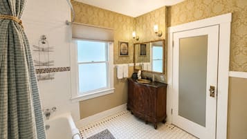 A bathroom with a bathtub, a vanity with a mirror, a shower, and patterned walls.