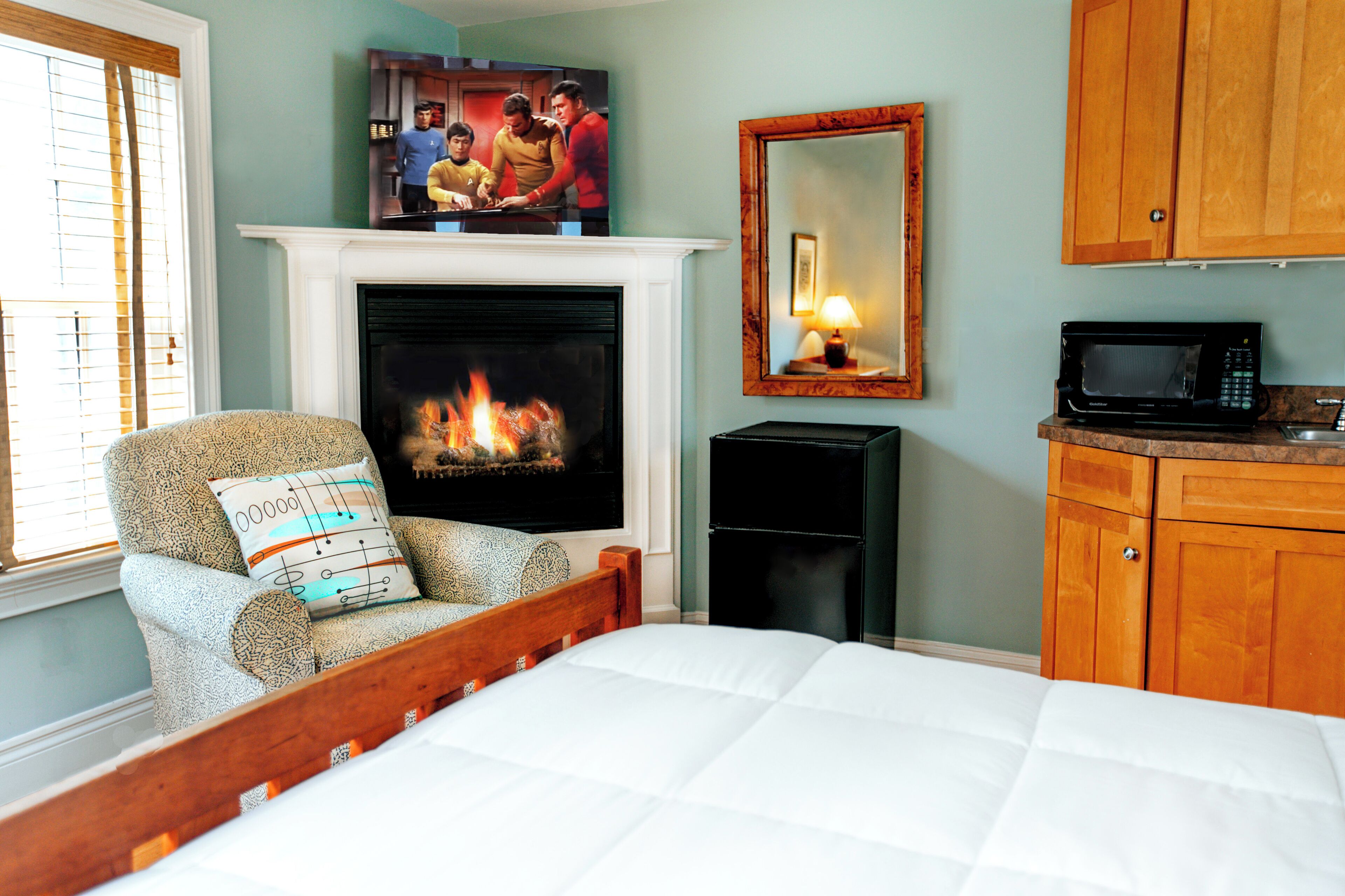 A bedroom with a fireplace, a bed, a chair, a television, a mirror, and wooden cabinets.