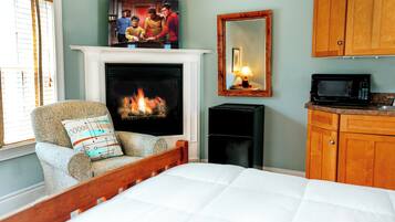 A bedroom with a fireplace, a bed, a chair, a television, a mirror, and wooden cabinets.