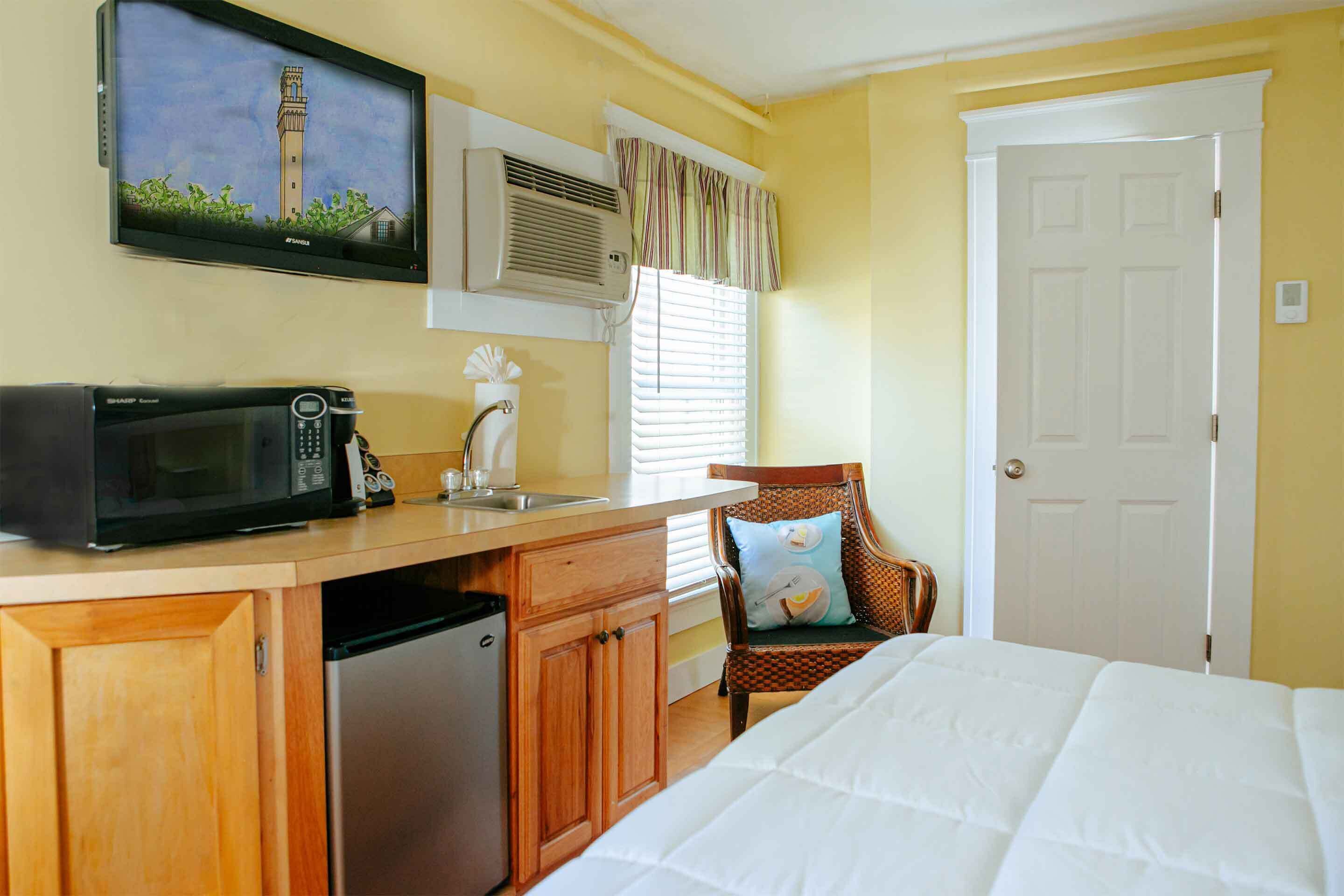 A compact hotel room with a kitchenette, a bed, a chair, and a door.
