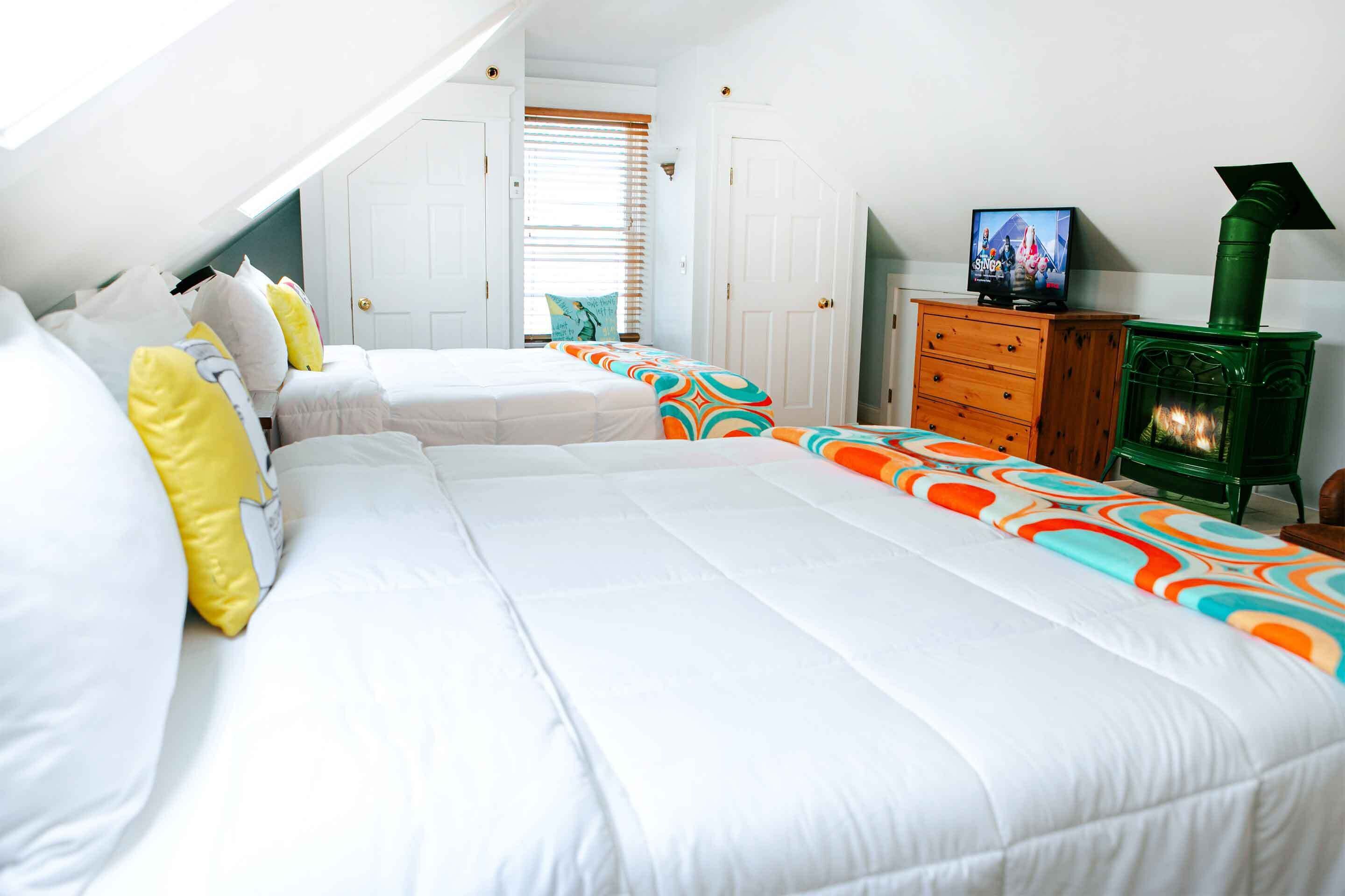 A bedroom with two beds, a wooden dresser, a television, and a green fireplace.